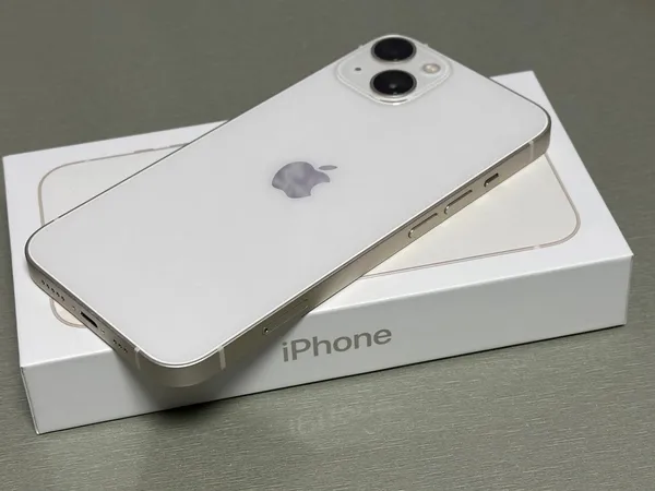 Apple iPhone 13 in starlight, rear view, resting on its retail box